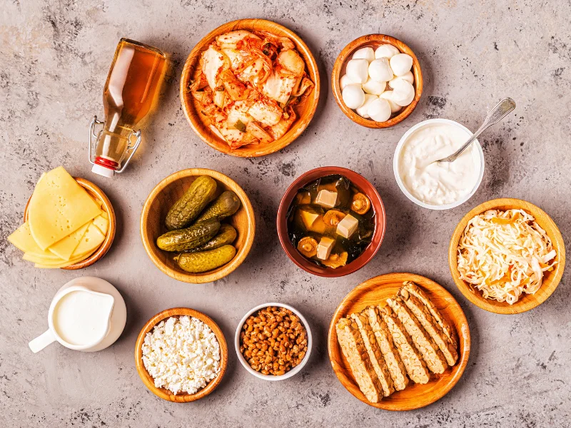 Fermented foods rich in vitamin k2 in wooden bowls on stone surface, including natto, sauerkraut, dairy products, and kombucha.