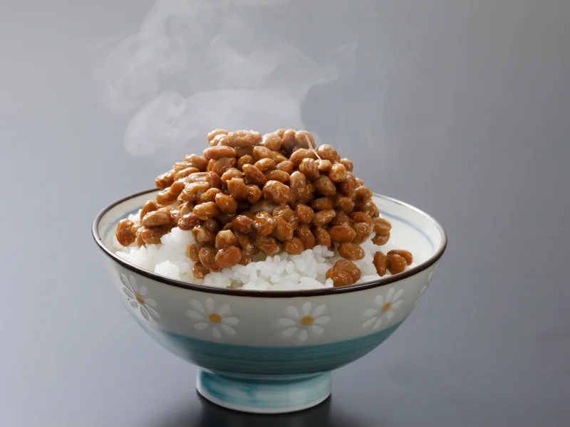 A bowl of natto, sticky fermented soybeans rich in vitamin k2, served over white rice with steam rising from the dish.